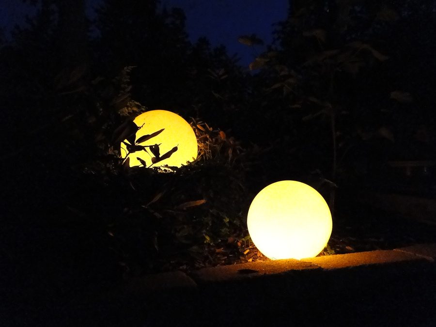 Zwei leuchtende Kugeln in einem Staudenbeet in der Dämmerung